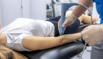 Editorial. A female patient lies on a therapy table while a physiotherapist applies ultrasound treatment with gel to the knee joint in a rehabilitation center. Bright clinic space with recovery and healthtech focus.